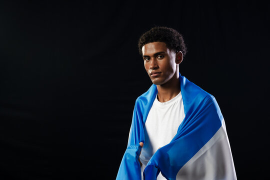 African American male standing wrapped in blue white flag wearing white tee in studio, copy space