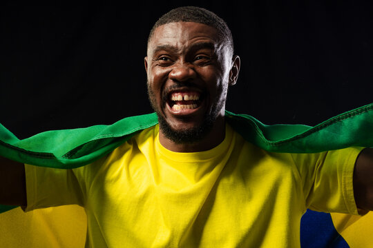 Mid-adult African man cheering and wearing yellow T-shirt while draping green fabric in studio