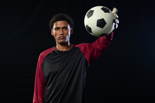 African American male goalkeeper holding soccer ball with gloved hand in studio in maroon jersey
