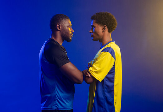 African male athletes standing arms crossed in studio wearing yellow-blue jersey and black shorts