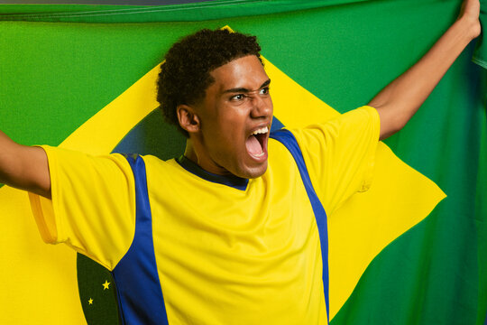 Man shouting while holding Brazilian flag and stretching yellow blue jersey in portrait studio