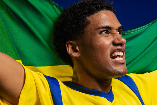 Male supporter shouting while holding green and yellow flag at stadium, wearing yellow jersey