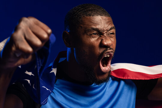 African American male shouting raising clenched fist wearing American flag and blue shirt in studio