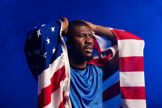 Mid adult African American man posing with American flag at studio wearing blue athletic shirt
