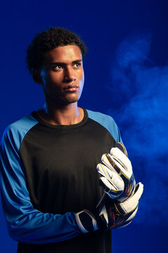 African man wearing goalkeeper jersey and adjusting white padded gloves in studio with smoke