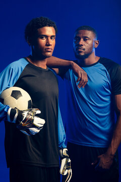 African American male teammates posing in studio, wearing goalkeeper gloves and holding soccer ball