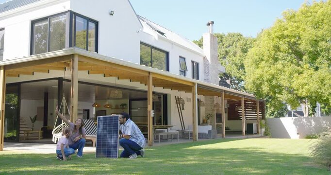 Family with teen placing solar panel on lawn, inspecting and planning roof install, copy space