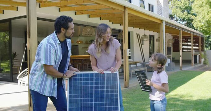 Family holding solar panel in yard, girl bringing mini panel, showing demo, man checking cable