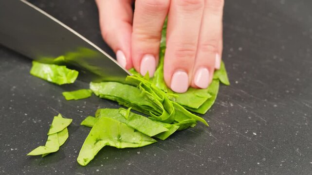 Glass bowl with chopped spinach and a board with onion and dill on a light blue background, top view. Cooking healthy vegan food
