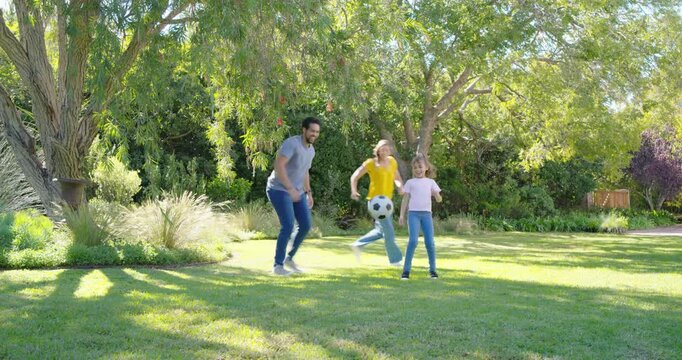 Family with child kicking soccer ball, parents passing and coaching while practicing skills on yard