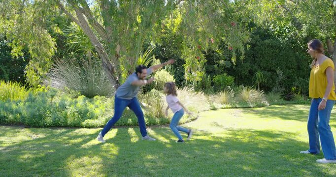 Family parents and child walking, adults gesturing then parents chasing, child running beneath tree
