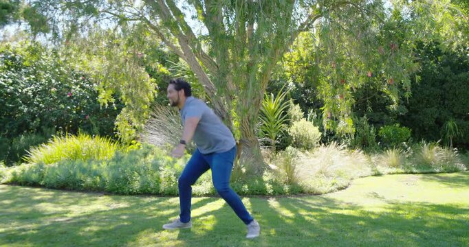 Diverse family playing chase around tree in yard, youth darting past woman in yellow, man lunging