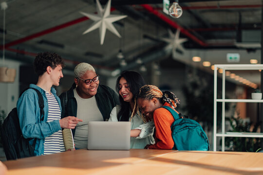 Diverse students collaborating on laptop, working together and learning in a modern library or university setting
