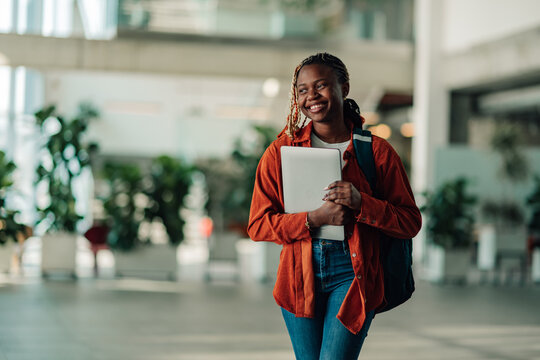 African american female student confidently walking on university campus, carrying a laptop and backpack