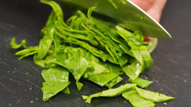 Glass bowl with chopped spinach and a board with onion and dill on a light blue background, top view. Cooking healthy vegan food
