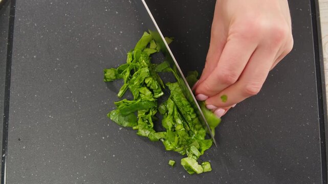 Glass bowl with chopped spinach and a board with onion and dill on a light blue background, top view. Cooking healthy vegan food
