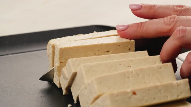 Chef cut cheese for Fried tofu with sesame seeds and spices on cast iron pan, cooking japanese salad. Healthy ingredient for cooking vegan vegetarian diet food. Roasted tofu over black background.