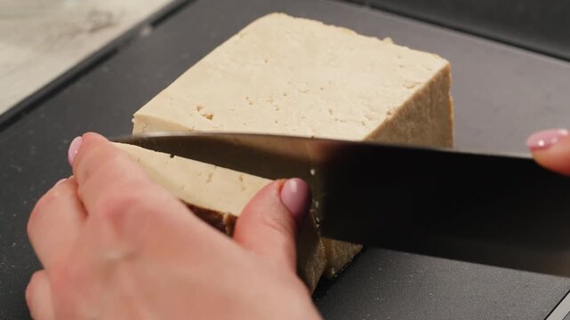 Chef cut cheese for Fried tofu with sesame seeds and spices on cast iron pan, cooking japanese salad. Healthy ingredient for cooking vegan vegetarian diet food. Roasted tofu over black background.