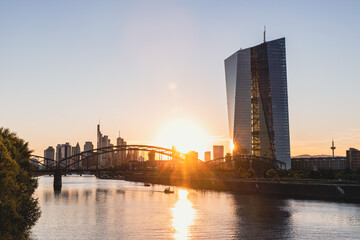 Moderne Banken-Architektur am Fluss bei Sonnenuntergang mit Stadtsilhouette und Hochhaus in Frankfurt © Marc Dyck