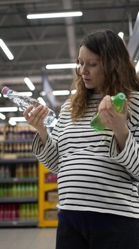 Expectant mother with a noticeable baby bump carefully reads labels on bottles in a supermarket aisle, choosing between a sugary soda and plain water for a healthier pregnancy