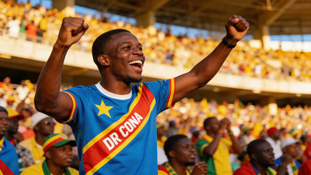 Cheering adult male fan raising both fists in stadium stands, wearing blue DR CONA jersey