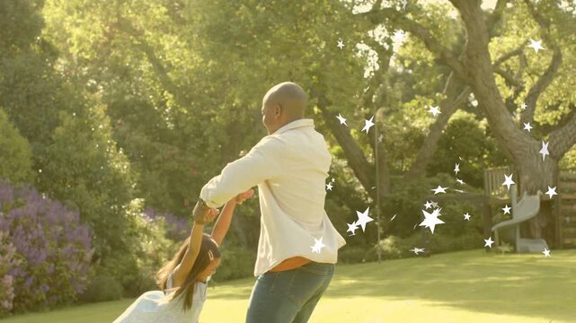 Man holding girl's hands in family yard, rotating her for play, white star overlay accenting motion