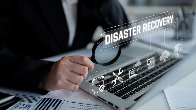 Businessman Analyzing Disaster Recovery Strategies with Technology Icons on a Laptop in a Modern Office Environment Sigmoid