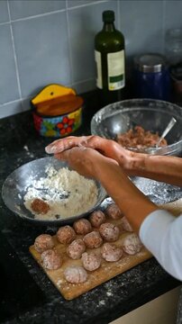 Vertical video of female hands shaping raw ground meat into meatballs with flour, homemade cooking process on wooden board, traditional Mediterranean recipe preparation, social media food content