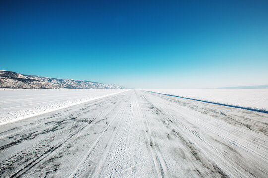 Snowy Road on a Frozen Lake in Winter With Clear Blue Sky and Distant Mountains Under Bright Sunlight