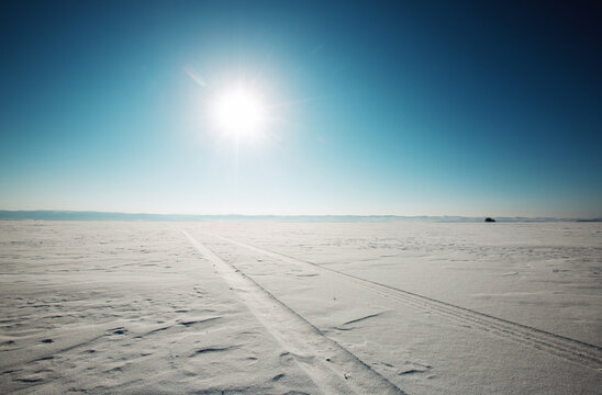 Wide Snowy Landscape With Tire Tracks Under Bright Sun on Clear Day in Winter Season