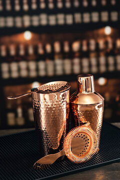 Shaker, strainer and mixing glass are on bar counter. Glossy surface. Classic accessories for bartender. Bar accessories are copper-colored. Black Bar mat. Copy space