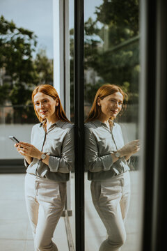 Woman enjoying a moment of reflection while using her smartphone indoors