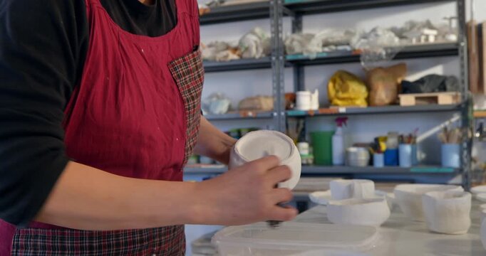 Crafting Pottery: A dedicated artisan meticulously molds and refines ceramic pieces within a well-equipped workshop. The artist's focus and passion are evident as she engages in her craft.