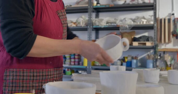 Crafting Moment: A focused individual in a workshop delicately handles pottery, showcasing artistic skill and attention to detail.