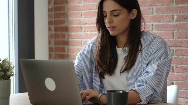 Tired freelancer woman feeling sleepy and yawning while working on her laptop from a modern home office, showing signs of exhaustion and overwork from a remote job on her computer