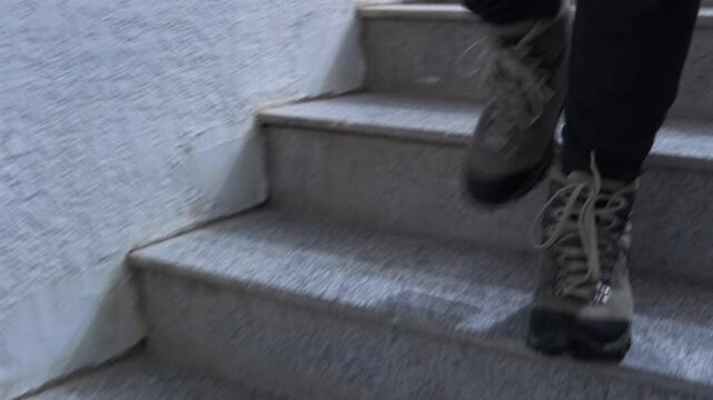 Front view of male legs in boots walking down entrance stairs, showing step motion, descent movement, indoor environment, everyday activity, footwear detail, human movement and urban routine