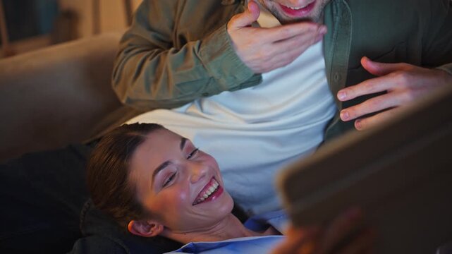 Laughing girlfriend watching tablet lying man knees closeup. Couple using tab