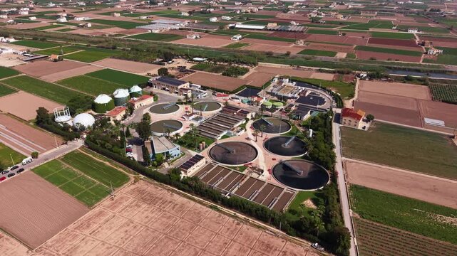 Aerial view of full-scale WWTP featuring circular secondary clarifiers, anaerobic digesters, biogas storage tanks, trickling filters, sludge treatment units and solar panels surrounded by agricultural