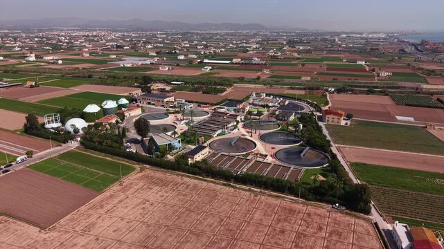 Aerial view of a modern WWTP showing circular secondary clarifiers, rectangular aeration basins, anaerobic digesters with biogas domes, sludge treatment units and agricultural surroundings in Spain