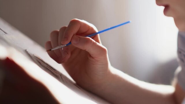 A teenager paints a paint-by-numbers picture on canvas with a brush. A boy dips a brush into paint and creates a creative drawing on a canvas. High quality FullHD footage