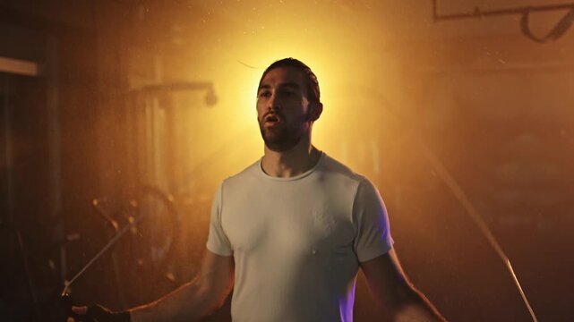 Determined muscular man jumping rope during a intense cardio workout in a hazy gym with backlighting