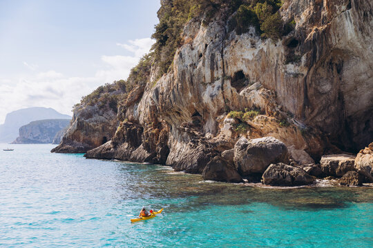 Person kayaking in turquoise water near Grotta del Bue Marino sea cave cliffs, Gulf of Orosei, Sardinia, Italy