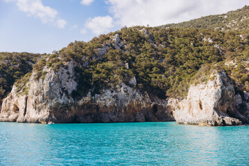 Naklejka premium Cala Luna beach in Sardinia, Italy, with turquoise water reaching rugged limestone cliffs and green Mediterranean vegetation
