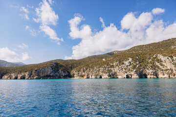Naklejka premium Cala Luna beach in the Gulf of Orosei, Sardinia, Italy with rugged limestone cliffs and sea caves under blue sky