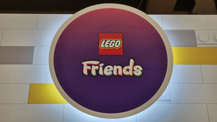 Naklejka premium A circular purple and pink gradient LEGO Friends logo sign with backlighting, centered on a white brick-patterned surface. Picture taken in April 27, 2026 in Bucharest, Romania.