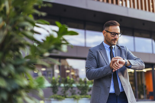 Businessman Checking Watch Outside Modern Office Building While Waiting For Meeting