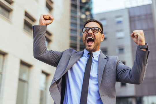 Excited Businessman Celebrating Success With Arms Raised Outside Corporate Office Building