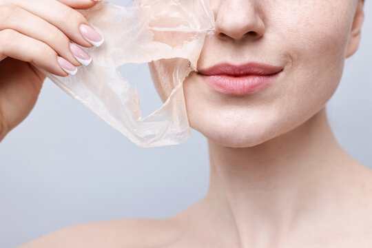 Beautiful woman peeling off facial mask on grey background, closeup