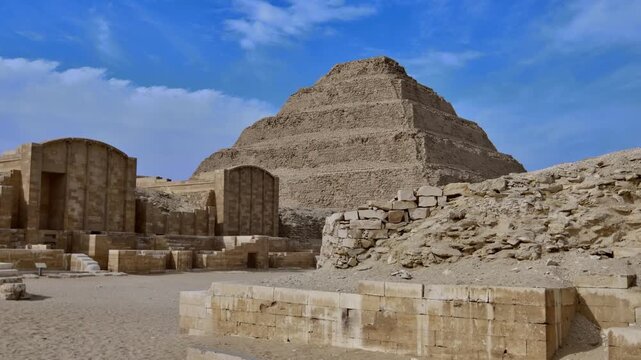 Exterior view of Djoser Step Pyramid at Saqqara, Egypt, oldest stone monument in the world, surrounded by ruins of funerary complex in sandy desert.