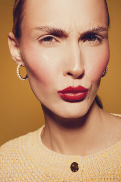 Close-up of a woman with red lipstick and pearl earrings making a skeptical face against a warm brown background. Concept of beauty, expression, fashion, and attitude.